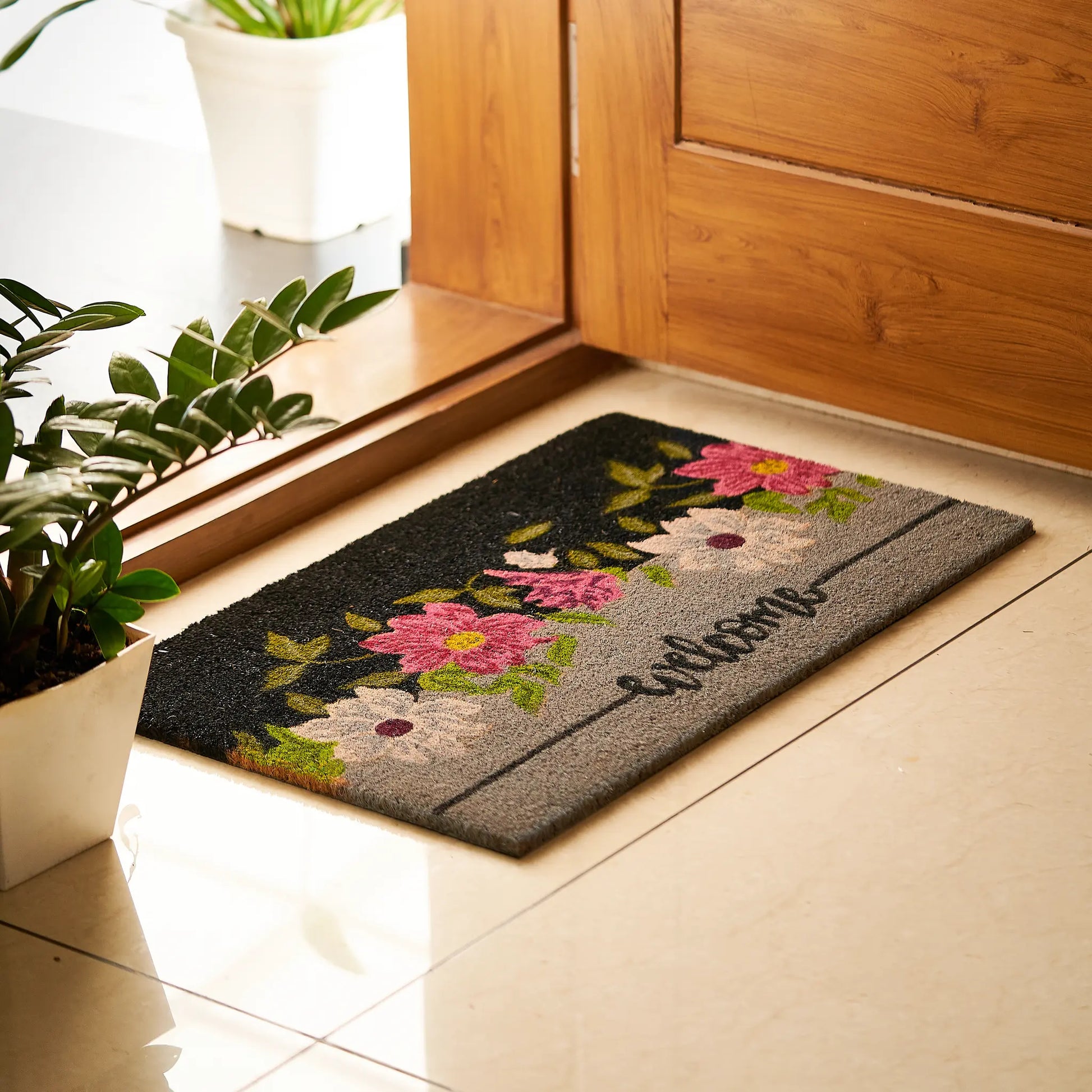 Decorative doormat with floral design and 'Welcome' text on a tiled floor.