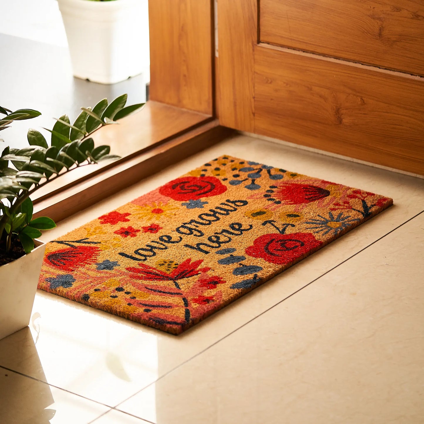 Decorative doormat with floral design and text on a tiled floor.