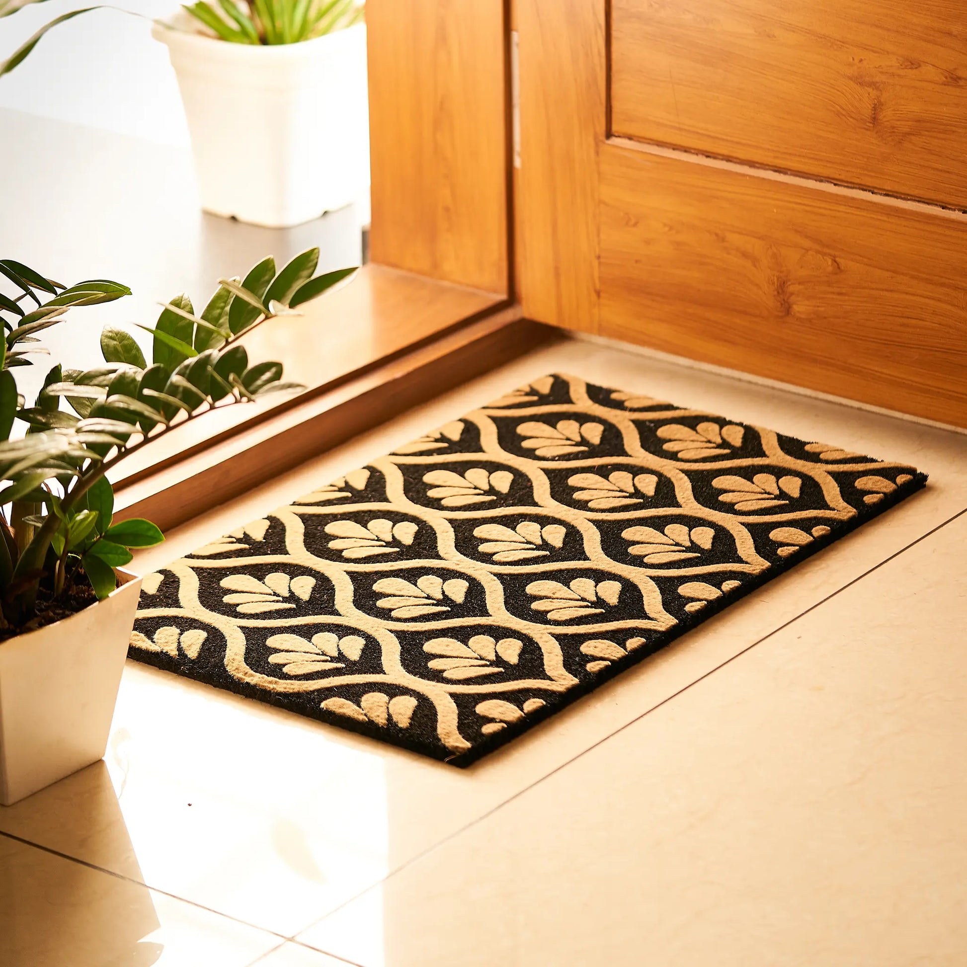Decorative doormat with leaf pattern on a wooden floor next to a door.