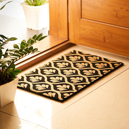 Decorative doormat with leaf pattern on a wooden floor next to a door.