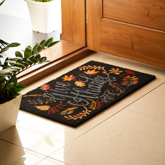 Decorative doormat with autumn design on a tiled floor next to a wooden door.