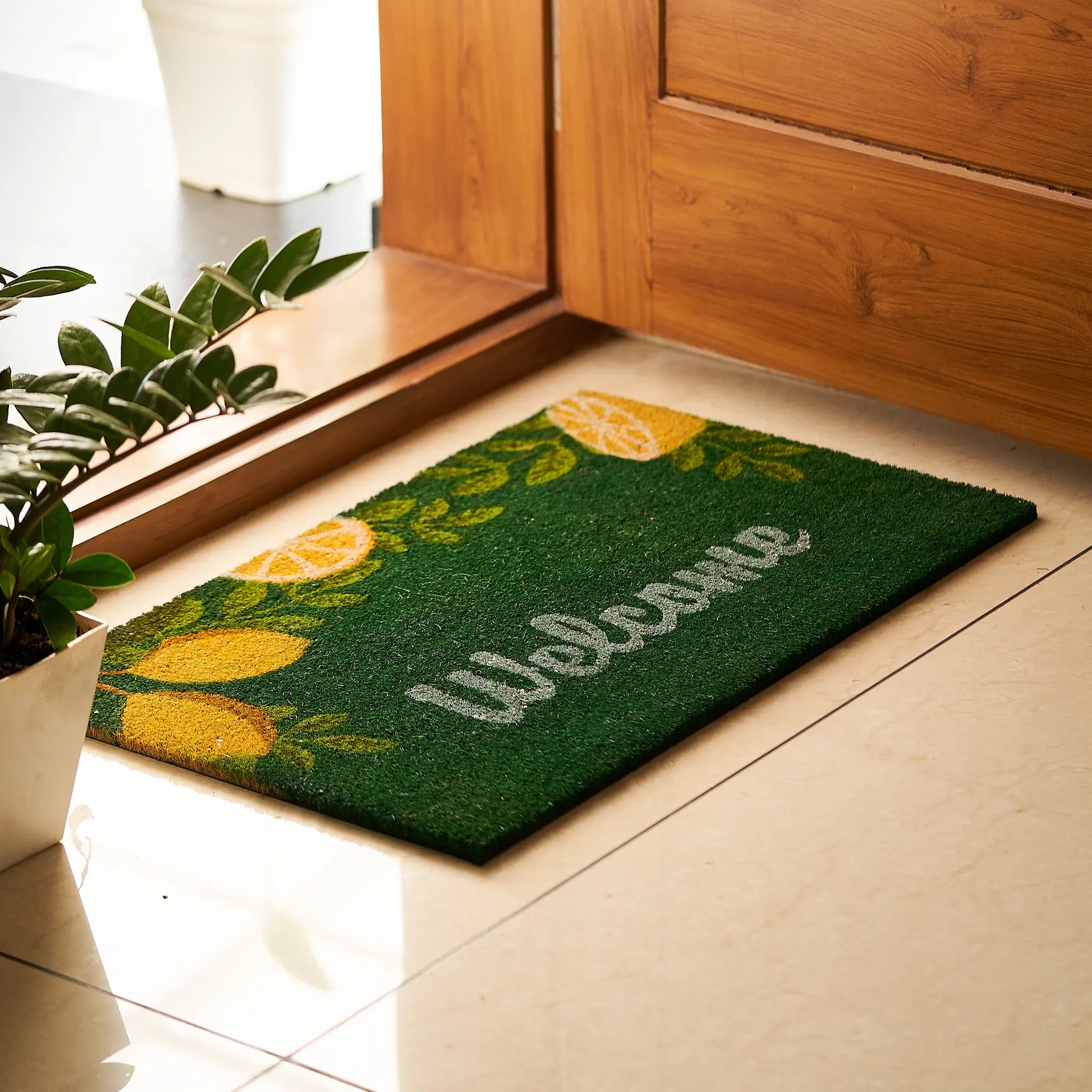 Green doormat with lemon design and 'Welcome' text on a wooden floor.